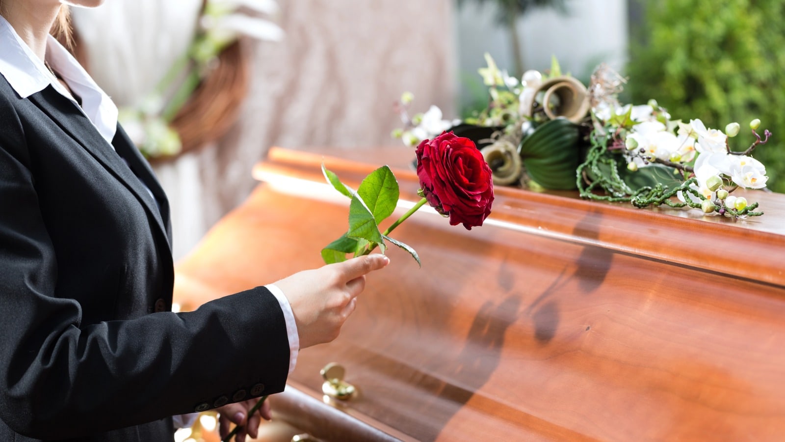 Una rosa rossa posata accanto alle composizioni floreali del commiato